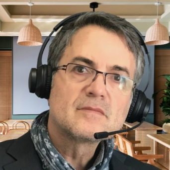 Mann mit Brille und Headset, trägt einen Schal und einen Anzug.
